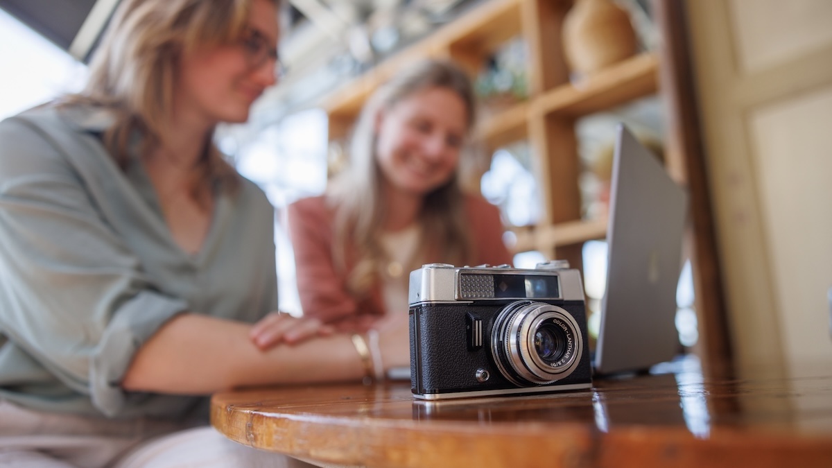 Sfeerbeeld van camera op de voorgrond met medewerkers op de achtergrond